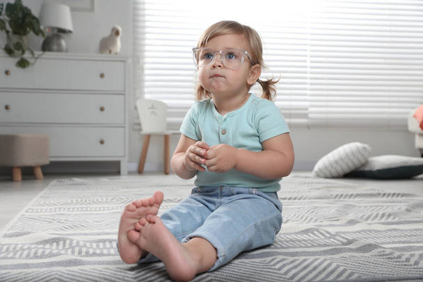 Cute little girl in glasses on floor at home - Фото, изображение