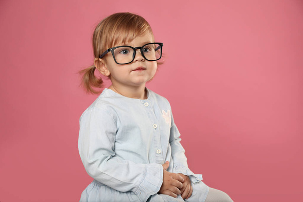 Cute little girl in glasses on pink background - Фото, изображение