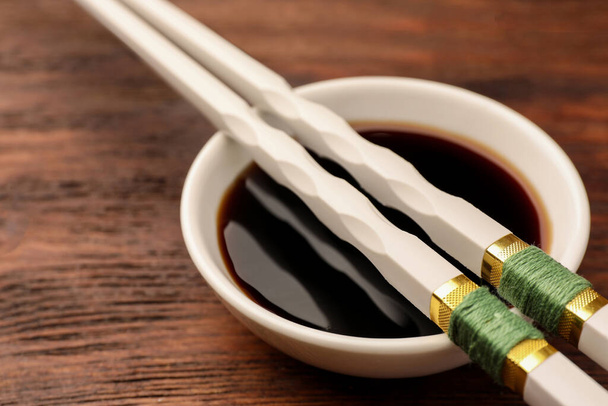 Bowl with soy sauce and chopsticks on wooden table, closeup - Foto, Imagem