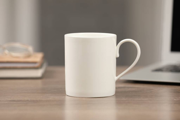 White ceramic mug on wooden table at workplace - Фото, изображение