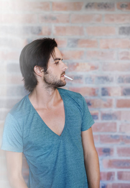 Hes got the James Dean vibe. Profile of an attractive man smoking against a brick wall with copyspace - Photo, Image