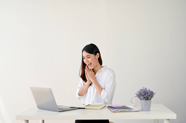 Una joven empresaria asiática sorprendida y emocionada o trabajadora de oficina está mirando la pantalla de su computadora portátil y sorprendida con buenas noticias. fondo aislado estudio blanco - Foto, Imagen