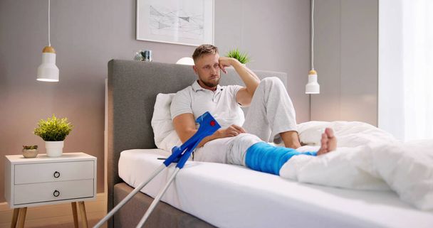 Injured Man With Broken Leg And Crutches In Bed - 写真・画像