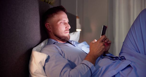 Muž v posteli s mobilním telefonem v noci - Fotografie, Obrázek