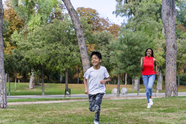 Szczęśliwy chłopiec bawiący się bieganiem z matką na świeżym powietrzu w parku. Koncepcja rodziny. - Zdjęcie, obraz