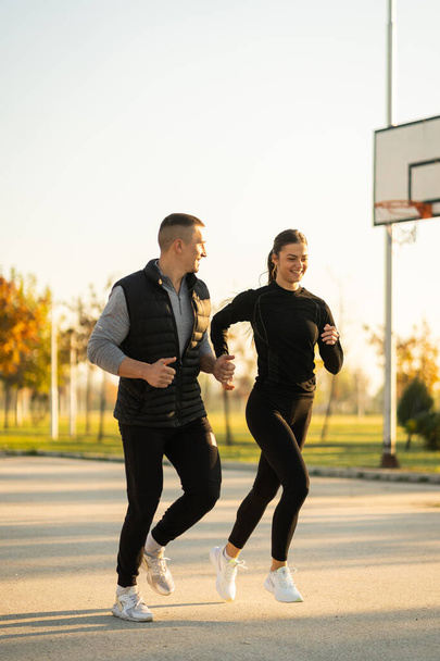 Два спортсмена в спортивной одежде бегают по парку и разговаривают - Фото, изображение