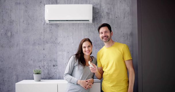Happy Young Couple Adjusting Temperature Of Air Conditioner By Remote - Foto, immagini