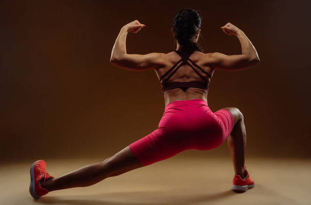 Foto de comprimento total da mulher forte esticando a perna esquerda enquanto mostra seu bíceps para a câmera - Foto, Imagem