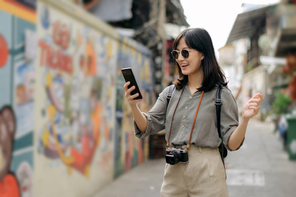 Joven mujer asiática mochila viajero usando el teléfono móvil, disfrutando de la calle cultural local arte pared. - Foto, imagen