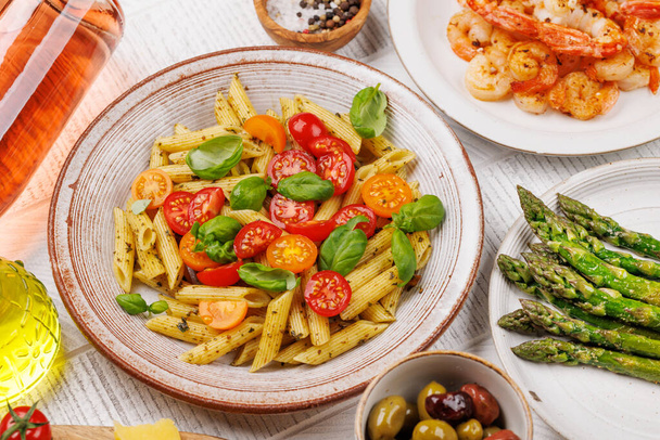 A delectable plate of Italian pasta adorned with fresh tomatoes and aromatic basil leaves, grilled asparagus and prawns - Фото, изображение