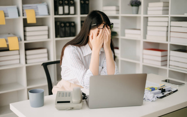 Asian woman feeling migraine head strain.Overworked businesswoman financier while working on laptop  at office. - Foto, imagen
