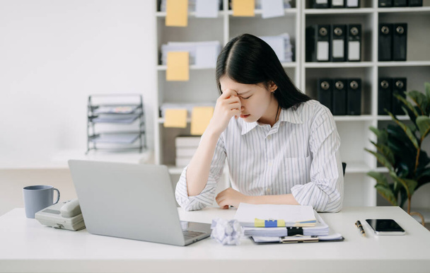 Mujer asiática sensación migraña cabeza strain.Overworked financiero mujer de negocios mientras trabajaba en el ordenador portátil en la oficina. - Foto, imagen