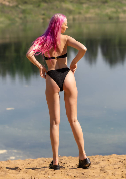 Sensual redhead girl in black swimsuit posing on sandy lake beach - Photo, Image