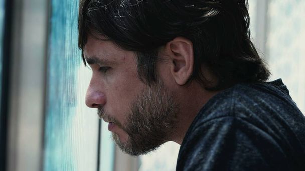Young man feeling regret leaning on window feeling despair. Hopeless male person in 30s feeling solitude and desperation - Фото, изображение