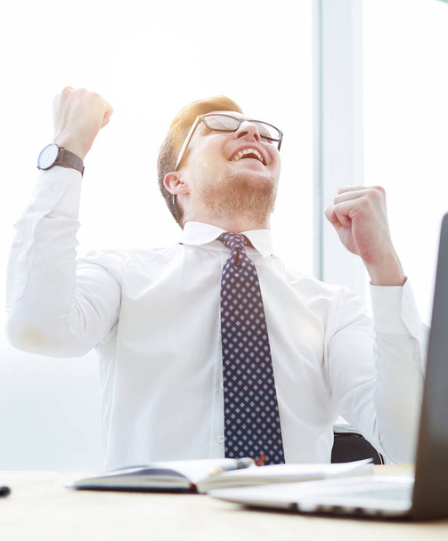 Happy young businessman raising hands in front of laptop - Фото, зображення