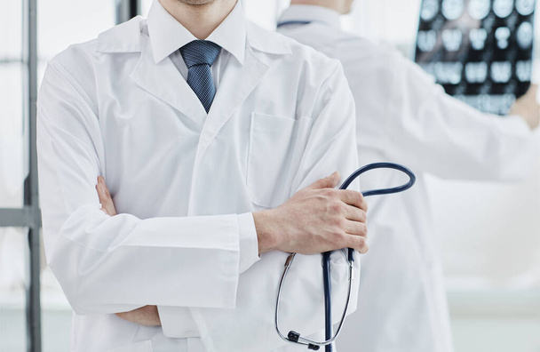 a doctor in a white coat and a stethoscope stands with his arms crossed - Foto, immagini