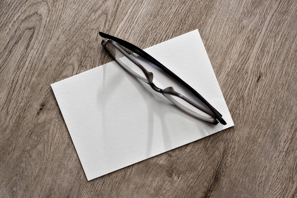 Tarjeta de papel blanco en blanco y lentes en blanco sobre un fondo de escritorio de madera beige neutro, maqueta minimalista de la marca de negocios con espacio para copiar - Foto, Imagen