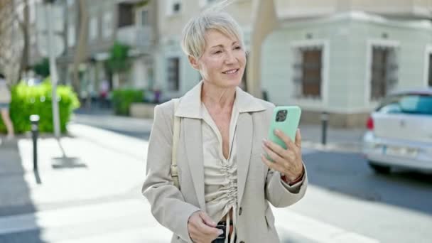 Middle age blonde woman dancing listening to music on smartphone at street - Footage, Video