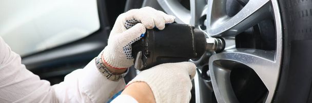 Garage master unscrews nuts to broken wheel of car. Tire service and auto service concept - Valokuva, kuva