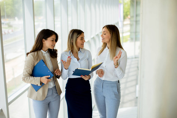 Three cute young business women having a discussion while walking in the office hallway - Photo, image