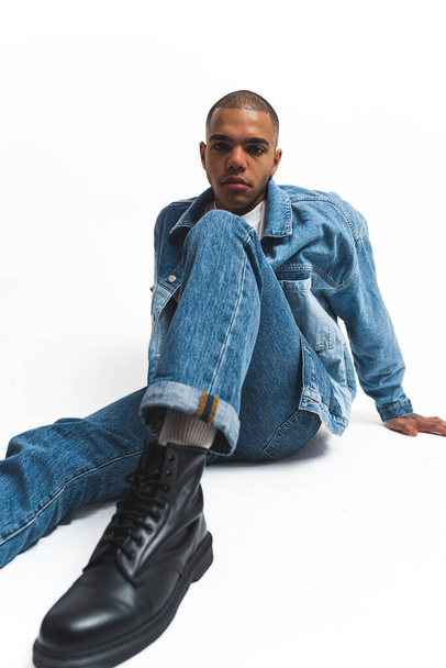 African American man in denim outfit striking pose with focus on his black shoes. High quality photo - Fotografie, Obrázek