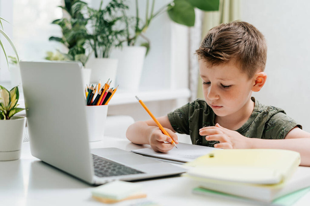 Улыбнись школьнику, занимающемуся дома с ноутбуком и делающему уроки. Думаю, кавказский ребенок сидит с блокнотом, карандашами и учебниками. Возвращайся в школу. Дистанционное обучение онлайн.  - Фото, изображение