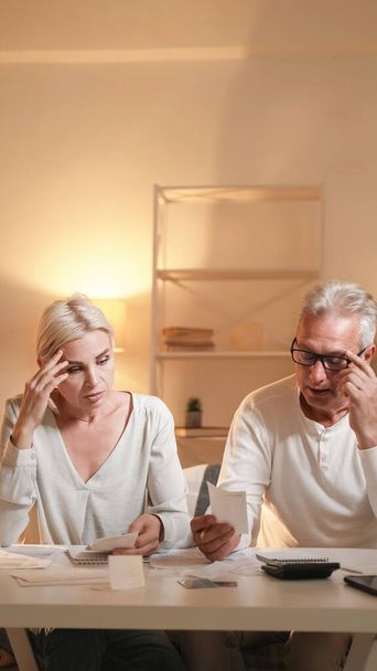 Budget problem. Middle-aged couple. Family finance. Disturbed husband and wife looking payment bills in light shadow room interior. - Fotoğraf, Görsel