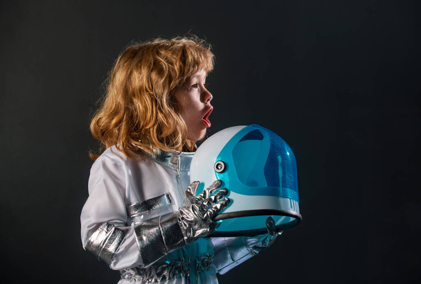 Cute little excited boy spaceman child in space suit holding helmet on black background - Fotoğraf, Görsel