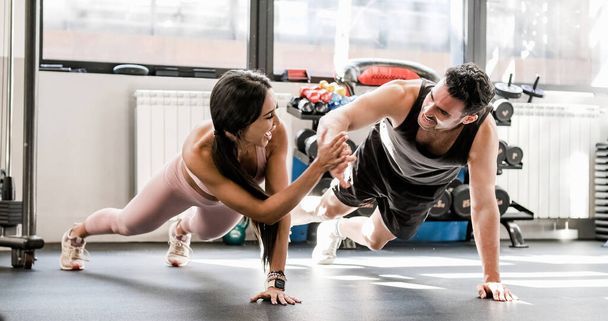 Full body of young strong positive woman and man athletes in sportswear smiling and giving high five while doing plank exercise during training in gym - Foto, Imagen
