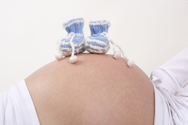 Raskaana oleva nainen, jolla on siniset vauvan kengät vatsassaan
 - Valokuva, kuva