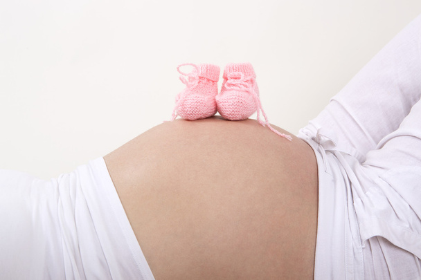 Zwangere vrouw met roze baby schoenen op haar buik - Foto, afbeelding