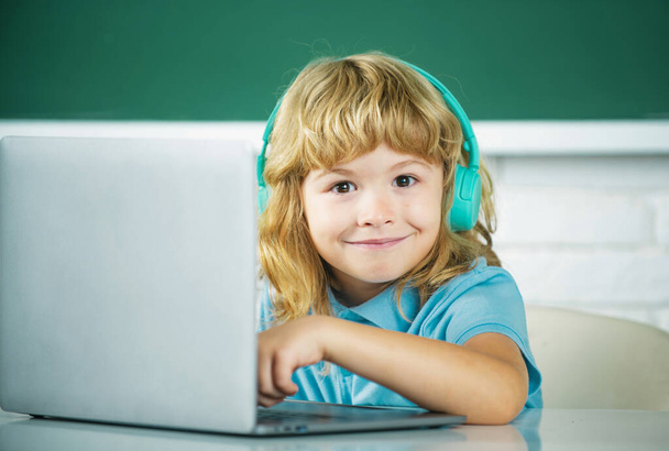 Funny school kid boy with laptop computer and headphones in class at school - Valokuva, kuva