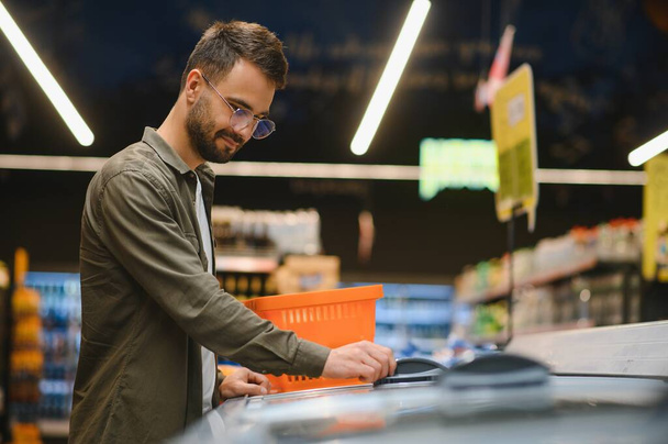 Young man buying groceries at the supermarket. Other customers in background. Consumerism concept - Photo, image
