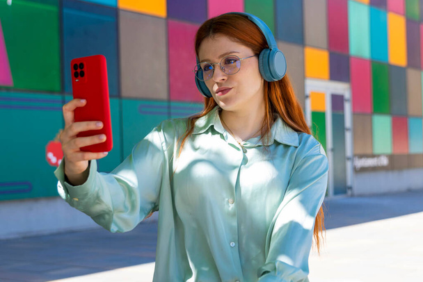 Redhead Girl. Rhythmic Delight: Stunning Redhead Enthralled by Music with Vibrant Mobile Phone - Foto, afbeelding