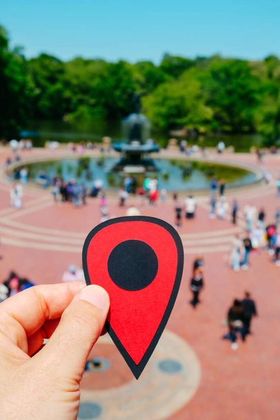 Рука чоловіка тримає червону позначку, що вказує на Терасу Бетесди в Центральному парку (Нью - Йорк, США) в сонячний весняний день. - Фото, зображення