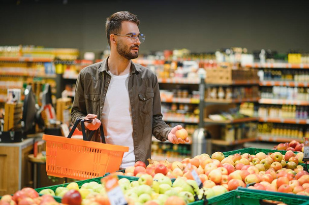 Чоловік купує овочі та фрукти в багаторазовому мішку в продуктовому магазині, концепція нульових відходів
. - Фото, зображення