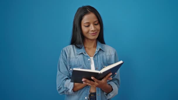 Mujer afroamericana leyendo libro haciendo gesto de pulgar hacia arriba sobre fondo azul aislado - Metraje, vídeo