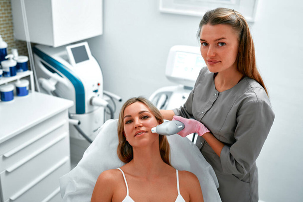 Zrelaksowany młody klient otrzymuje SMAS ultradźwiękowy masaż twarzy z profesjonalnym sprzętem w centrum urody. Niechirurgiczny lifting twarzy. Obróbka skóry za pomocą urządzenia laserowego. - Zdjęcie, obraz