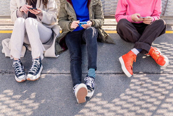 trzech nierozpoznawalnych przyjaciół siedzących na podłodze przewijających się razem przez media społecznościowe z telefonem komórkowym, koncepcją przyjaźni i nowoczesnym stylem życia - Zdjęcie, obraz