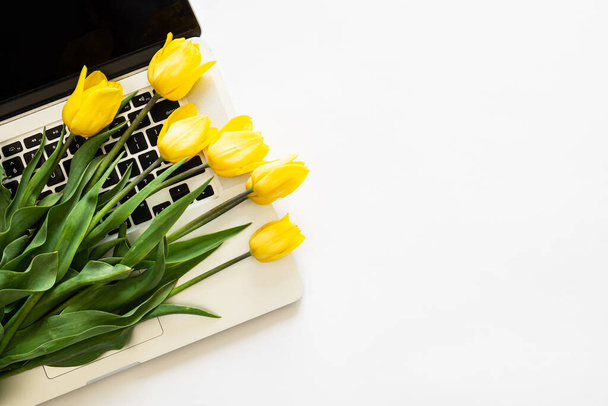 Bir buket sarı parlak lale ve beyaz zemin üzerinde bir laptop izole edilmiş, üst görünüm, metin için boşluk. - Fotoğraf, Görsel
