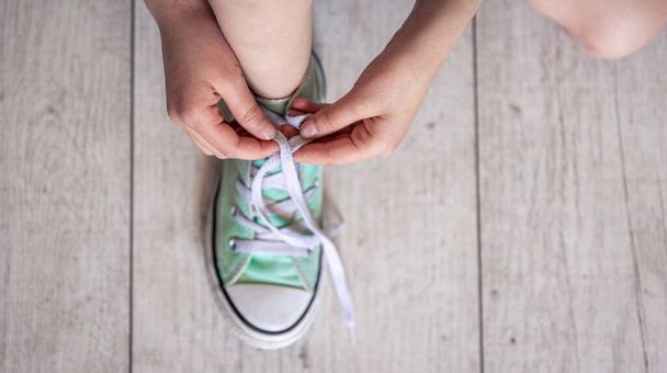 Child successfully ties shoes, close up on feet, child ties shoelaces on sneakers, top view. - Photo, Image