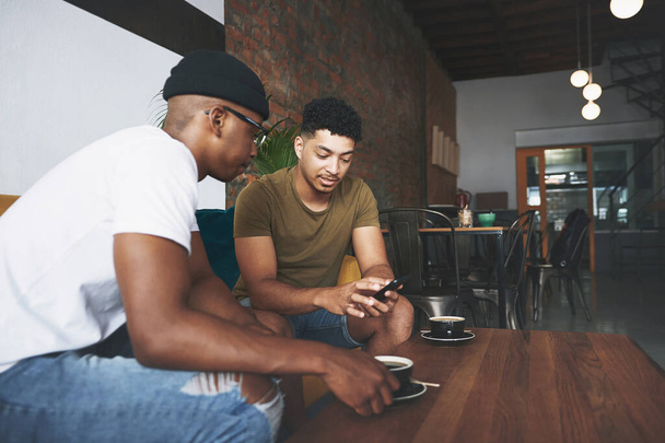 Déjame mostrarte una foto... hombres discutiendo algo en un celular mientras están sentados juntos en una cafetería - Foto, imagen