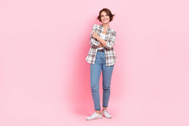 Full length photo of funky adorable woman dressed plaid shirt pointing finger empty space isolated pink color background. - Foto, Bild