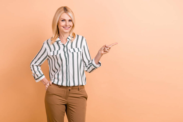 Photo of pleasant senior woman with bob hairstyle striped shirt arm in pocket directing at empty space isolated on pastel color background. - Фото, зображення