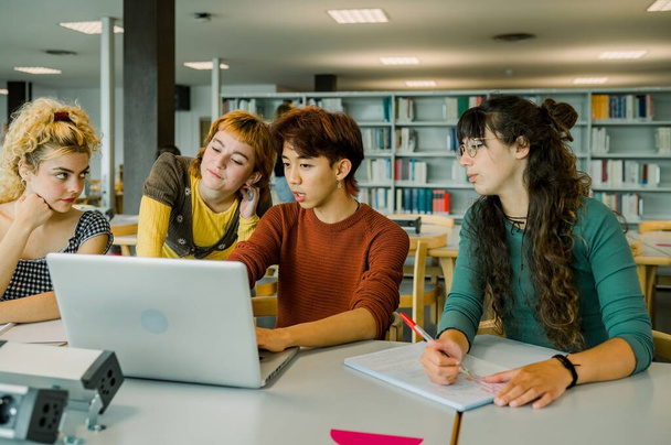 Groupe d'amis étudiants multiraciaux assis à la table dans la bibliothèque regardant l'écran de l'ordinateur portable et asiatique mâle expliquant le projet tandis que la blonde féminine penchant sur la main et regardant loin - Photo, image