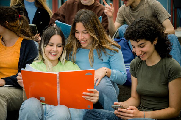 Ryhmä onnellinen monikansallinen college ystäviä oppikirjoja ja älypuhelin valmistautuu testi ja hymyillen opiskellessaan yhdessä penkeillä - Valokuva, kuva