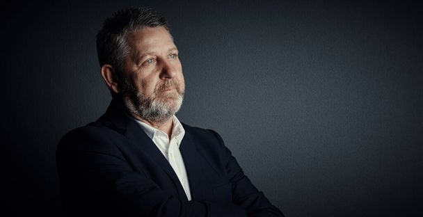 Thinking about his corporate future. Studio shot of a handsome mature businessman looking thoughtful while standing against a dark background - Foto, imagen