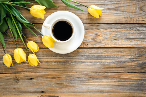 Strauß leuchtend gelber Tulpen und Tasse schwarzen Kaffees auf einem Holzhintergrund, Draufsicht, Kopierraum. - Foto, Bild