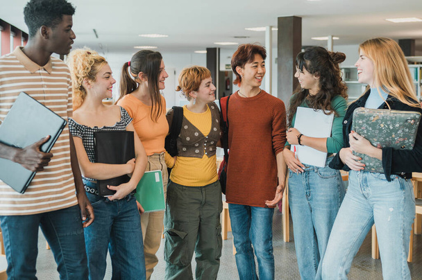 Veselý multiracial dospívající studenti s notebookem a dopisní s úsměvem a při pohledu na sebe při setkání ke studiu v knihovně moderní univerzity - Fotografie, Obrázek