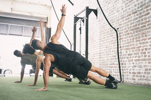 Améliorez votre équilibre corporel. un groupe de fitness faisant la planche latérale ensemble au gymnase - Photo, image